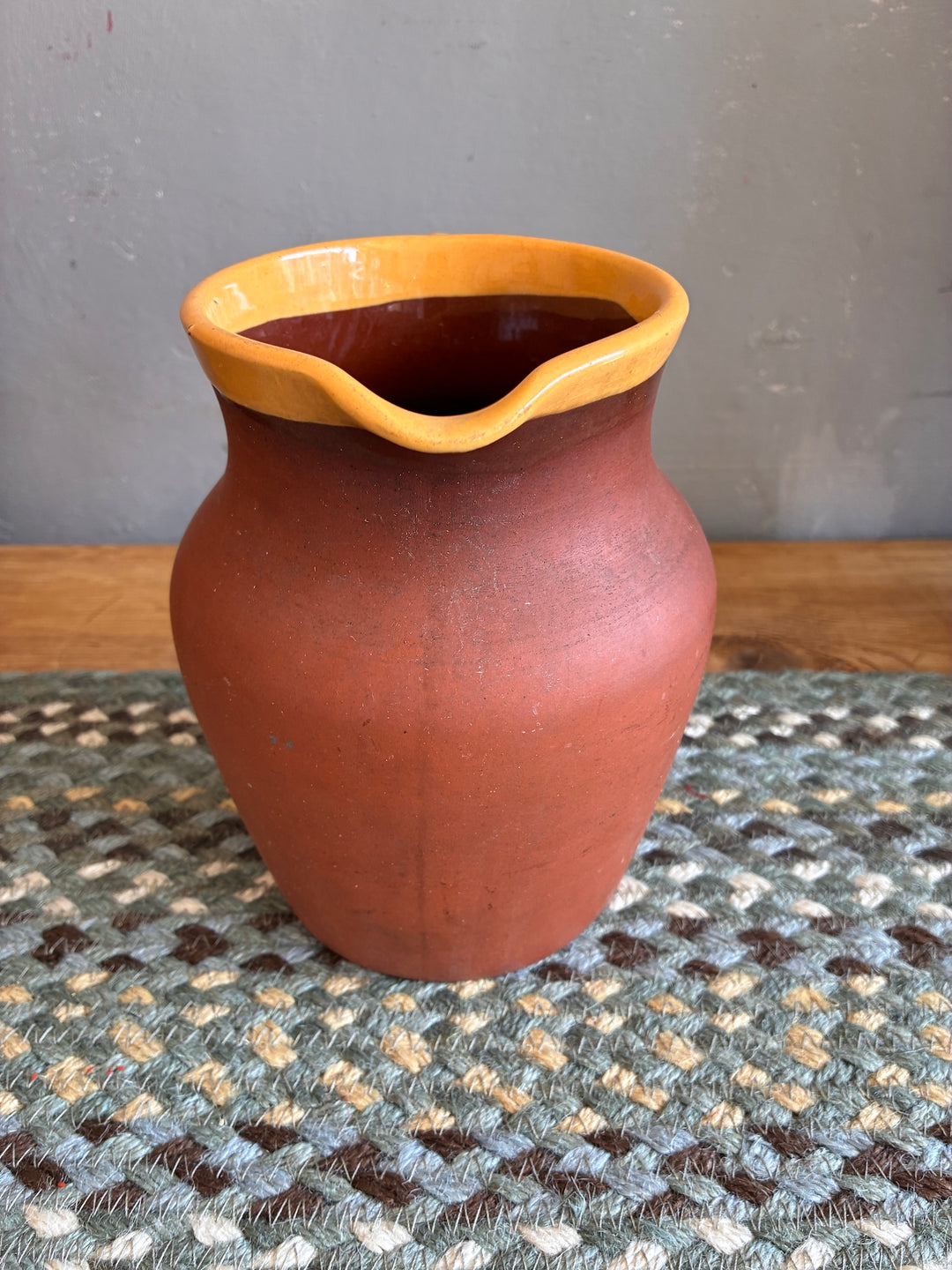 Vintage Terracotta Jug - Yellow Glaze Rim displayed on a woven rug, showcasing rustic charm and unique craftsmanship.