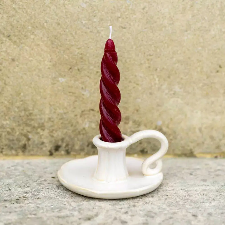 Vintage white ceramic candle holder with a red twisted candle on a stone surface