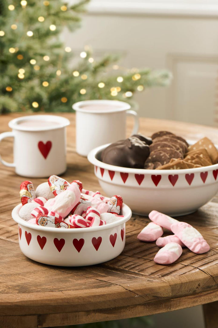 Pretty White Enamel Bowl with Red Heart Design filled with candies, next to mugs and a Christmas tree.