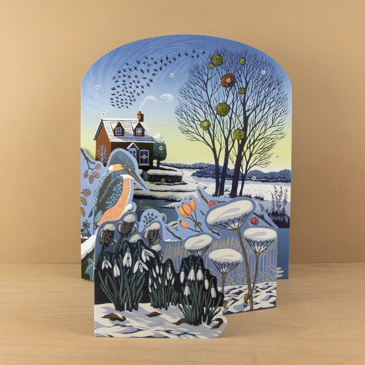 Winter Riverside Advent 2026 Calendar - Niki Bowers featuring a cozy winter scene with a cottage and snow-covered landscape.